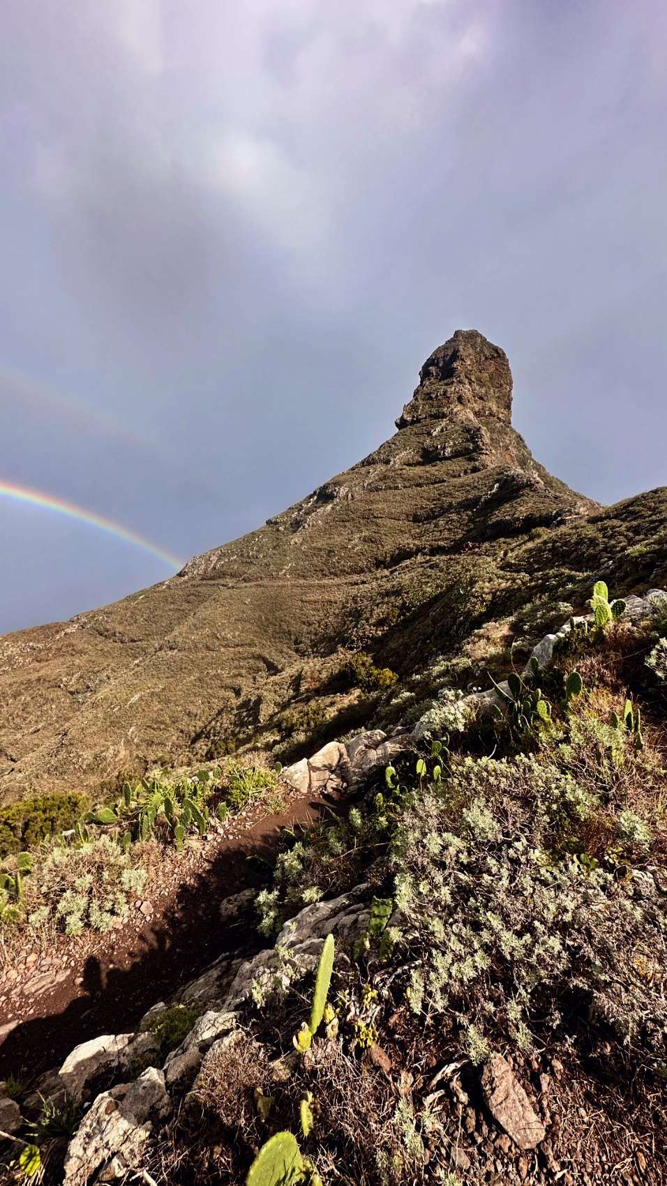 The sharp rock tower of Roque de Taborno with a rainbow arching behind it.