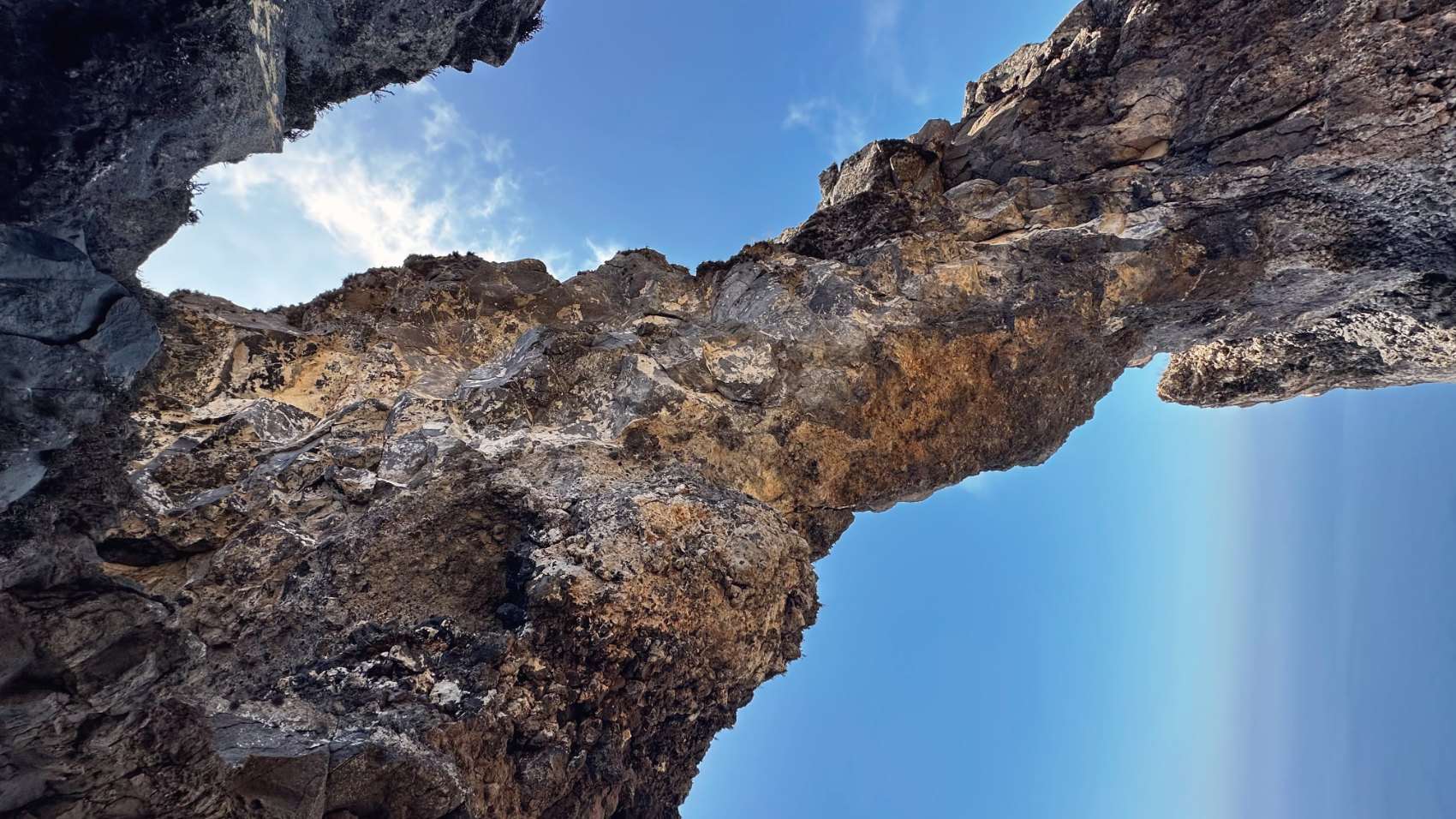 A natural arch of volcanic rock photographed from below against a blue sky.