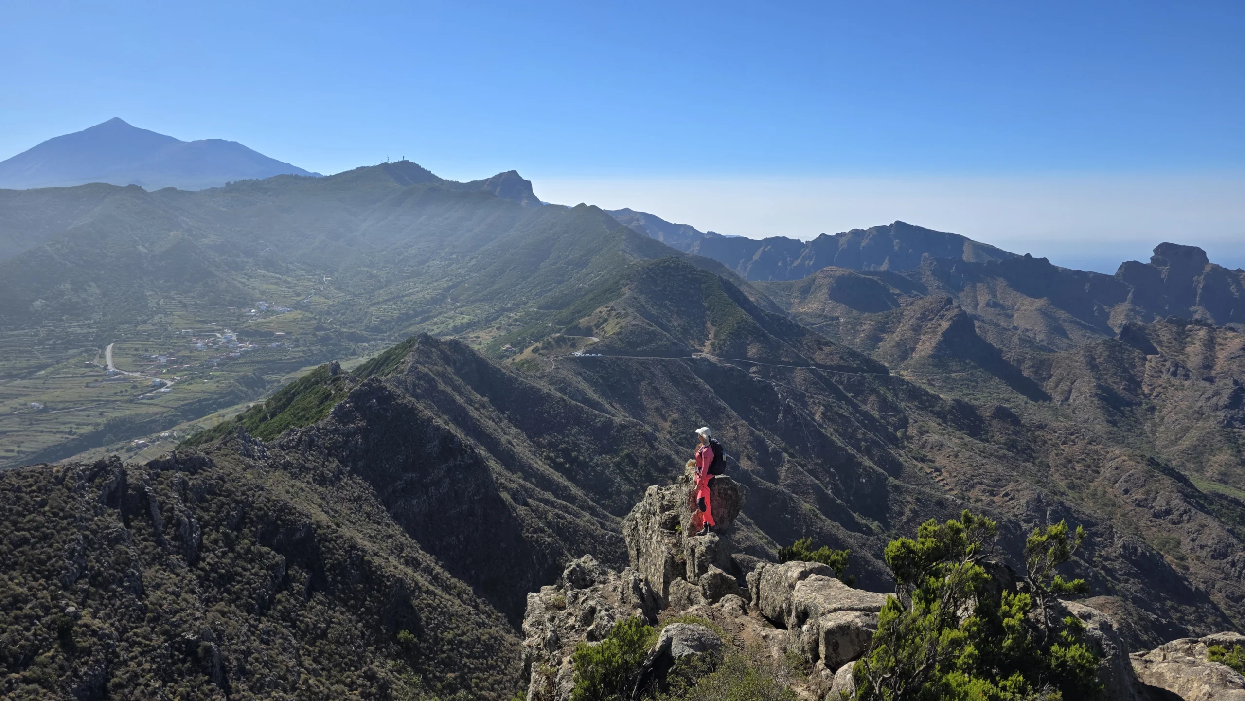 A hiker on a rocky outcrop above the ridges and valleys of Teno, with Teide on the horizon, Tenerife.