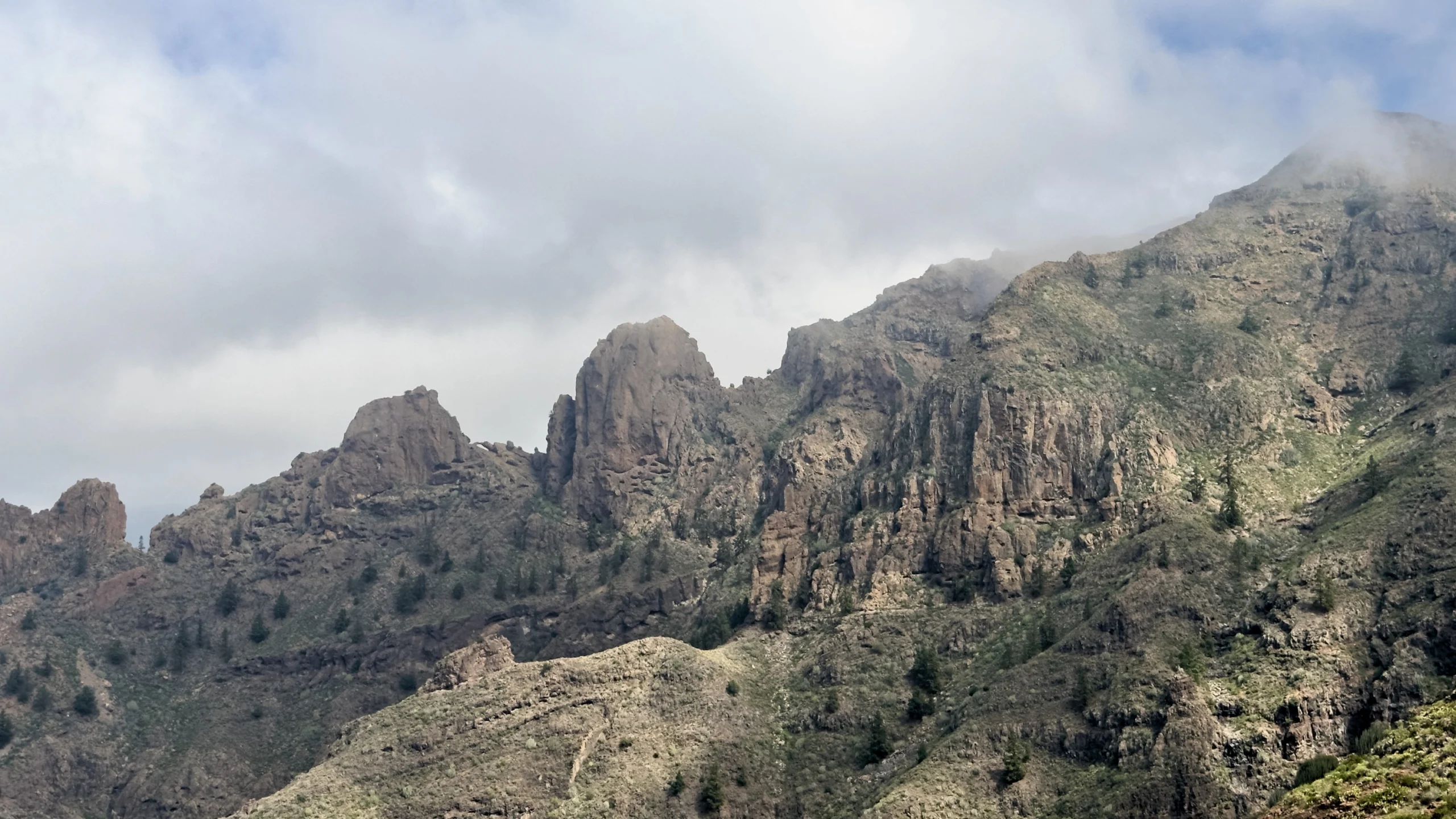 Volcanic rock towers rise above a green ravine under the clouds, Ifonche.